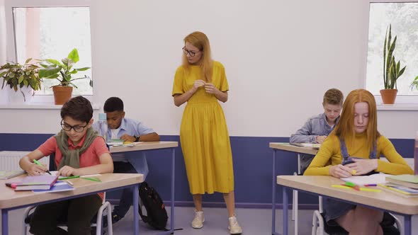 Female Teacher Helps Hardworking Students Writing a Test in Elementary School