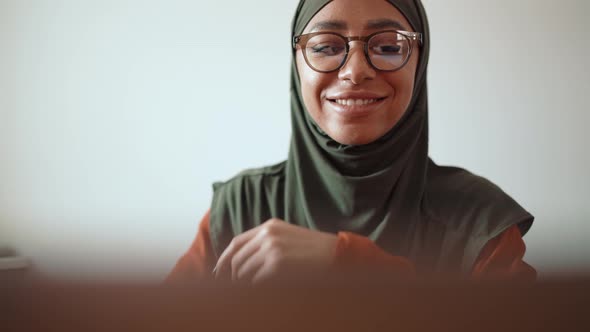 Happy young Muslim woman wearing eyeglasses working on laptop