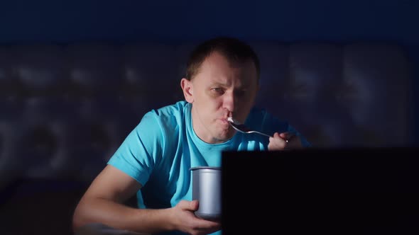 Young man eating ice cream at night and watching TV, camera movement