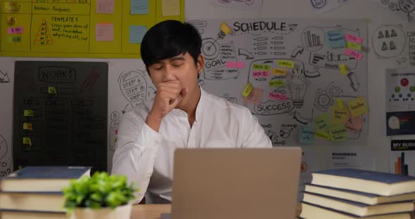 Sleepy businessman sits at workplace desk with a laptop working