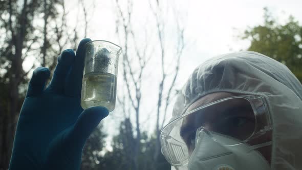 Chemist in Ppe Looking at Flask with Solution Water Analysis From Swamp Wearing Protective Suit and