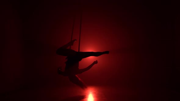 Silhouette Aerialist Girl Doing Acrobatic and Flexible Tricks on Red Aerial Silks or Tissues on Red