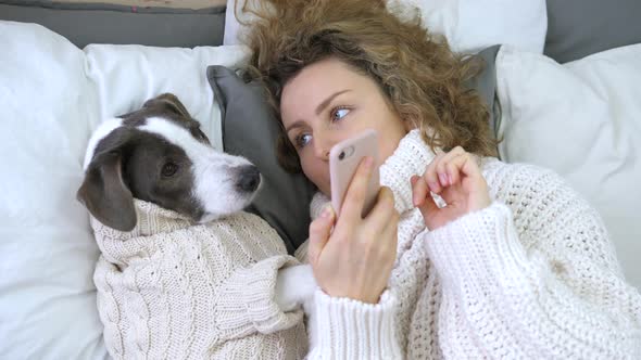 Woman Teaching Her Dog How To Use A Smartphone Lying In Bed