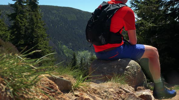 Young Man Sits on the Stone in the Middle Pathway To the Top of the Mountain and Looks Around