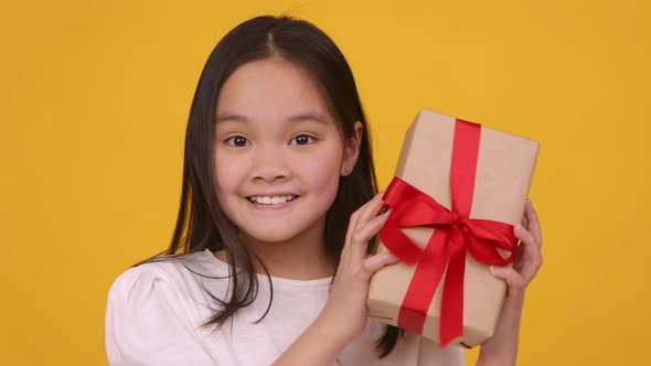 Cute Asian Girl Shaking Gift Box Trying To Catch What's Inside Orange Background Slow Motion