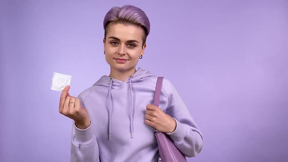 Positive Young Woman Showing Condom Putting in Handbag Isolated