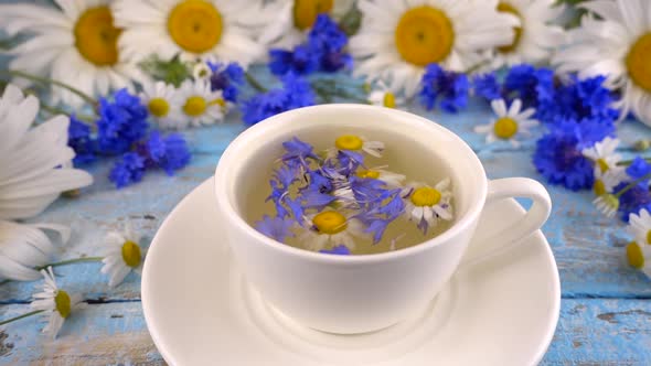 Brewing a tisanes from knapweeds and chamomile in white cup.