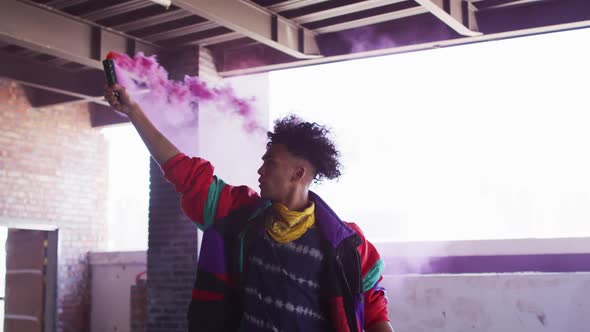 Mixed race man holding purple flare standing in an empty building