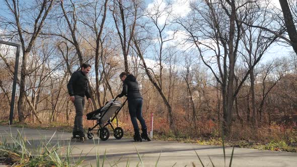 Sport Young Parents Roller Skate with Their Baby in a Stroller in a City Park. Autumn, Sunny Day