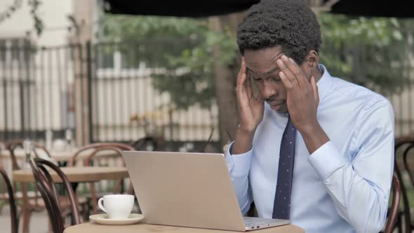 Pensive African Businessman Working on Laptop in Outdoor Cafe