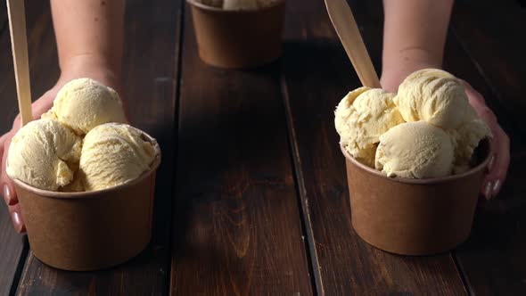 Femalie Hands Placing Three Vanilla Ice Cream Cups on Wooden Table