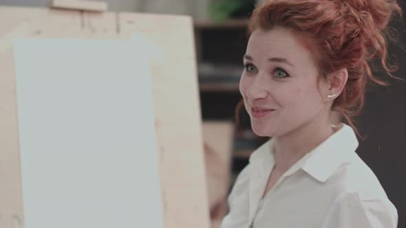 Young Female Painter Near Easel Describing Creative Process