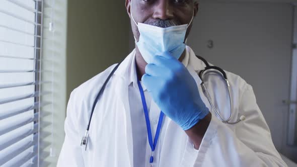 Portrait of smiling african american male doctor wearing face mask standing in hospital room