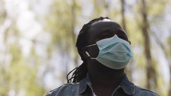 Portrait Shot of an African Man with Medical Mask and Wireless Headphones in the Nature