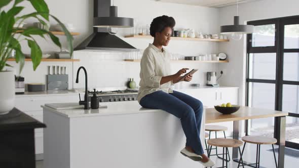 Happy african american woman using smartphone in kitchen