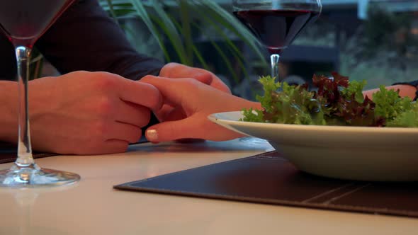 Male Hands Hold and Caress a Female Hand Across a Table with Meal and Wine