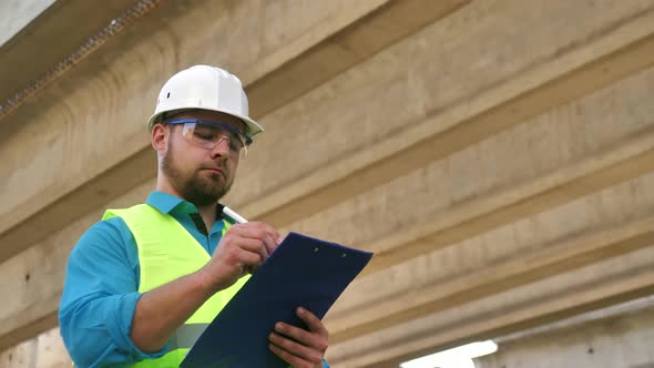 A Male Builder in a Hard Hat at the Urban Construction Site of a New Residential Complex