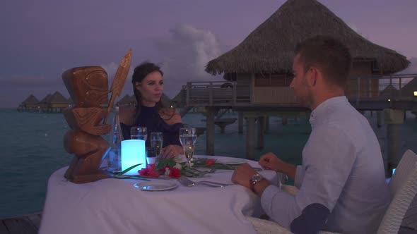A man and woman couple dining on a deck pier at night in Bora Bora tropical island