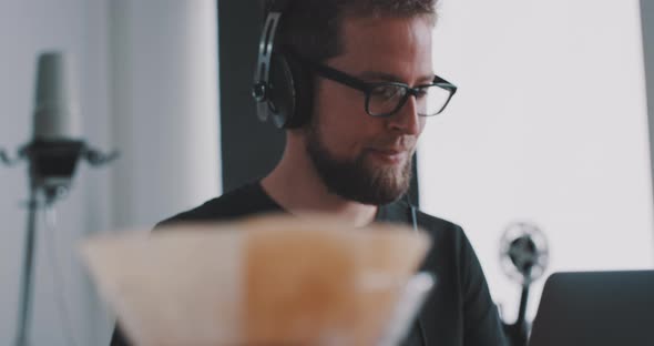 A young man with headphones prepares coffee at desk