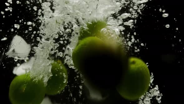 Closeup of Falling Ripe Limes and Ice Into the Sparkling Water on Black Background Making a Cocktail