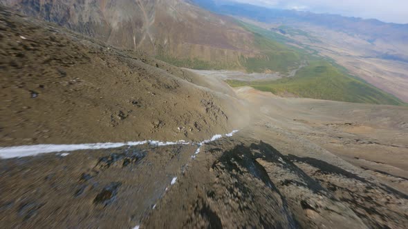 Aerial View Dive Movement From Snowy Mountain Summit to Natural River Creek Endless Valley Landscape