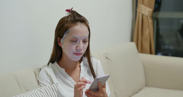 Woman use of mobile phone with paper mask at home in the evening