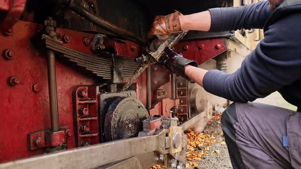 Mechanic adding oil in mechanisms of the stopped steam train Mocanita on a railway station in Romani