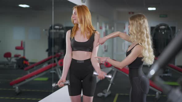 Portrait of Motivated Young Redhead Woman Lifting Dumbbells As Blond Individual Trainer Supporting