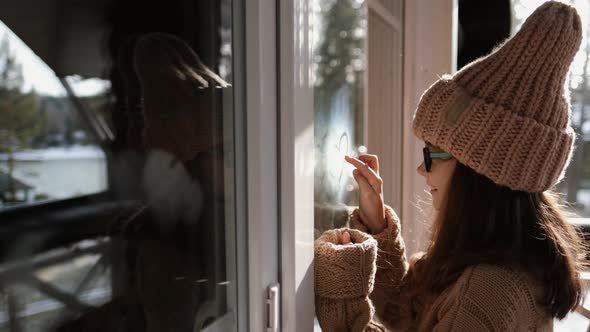 Little Girl in a Sweater Draws a Heart in Condensation on a Balcony Window