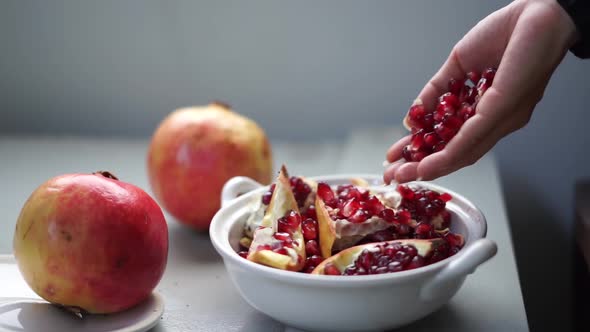 Close-up of female hand putting pomegranate seeds in a white bowl. Vegetarian food without dairy or