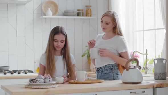 Teen Girl Schoolgirl Daughter Pours Sugar Into Cup with Tea Standing in Kitchen at Home with Mom