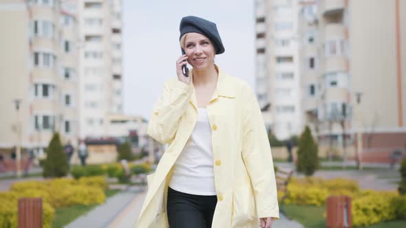 Happy Positive Woman Walking Along the Alley in Residential Complex and Talking on the Phone