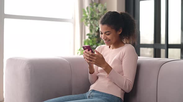 An Attractive Young AfricanAmerican Woman Using a Smartphone at Home
