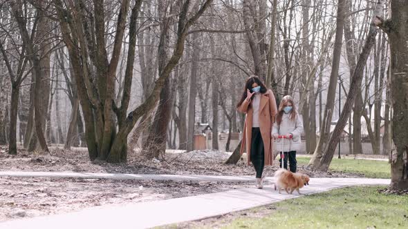 European Mother and Her Daughter in Masks Are in a Park with a Dog