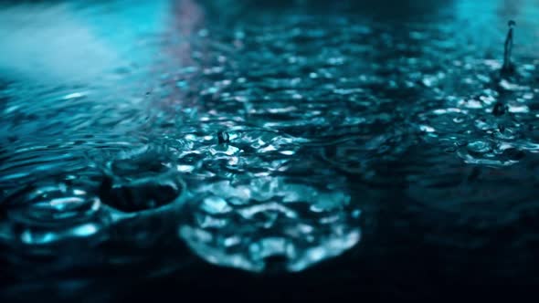 Slow Motion of Rain Drops Falling Into Puddle on Asphalt at Night. Big Modern City Lights Mirror