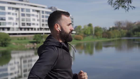 Adult Man Runs in the Park Near the City Camera Following Runner in Wireless Headphones Healthy