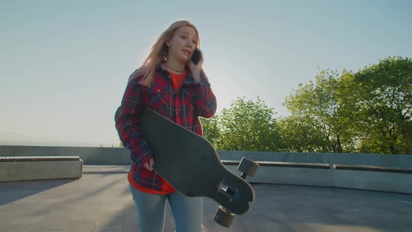 Pretty Hipster Woman with Longboard Skateboard Talking on Cellphone