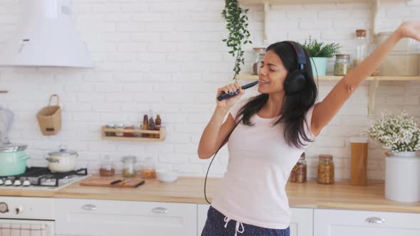 Young Happy Woman Dancing and Singing in Kitchen in Headphones and Having Some Fun