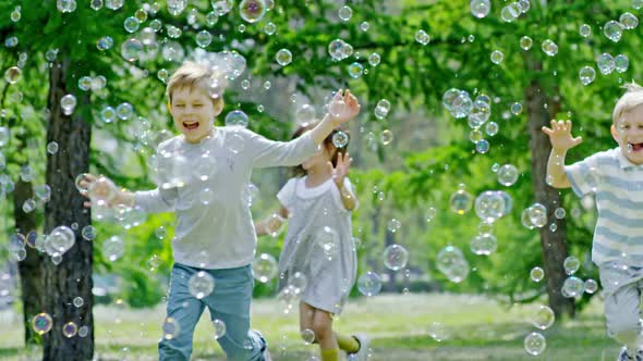 Excited Children Running through Lots of Soap Bubbles in Park alt