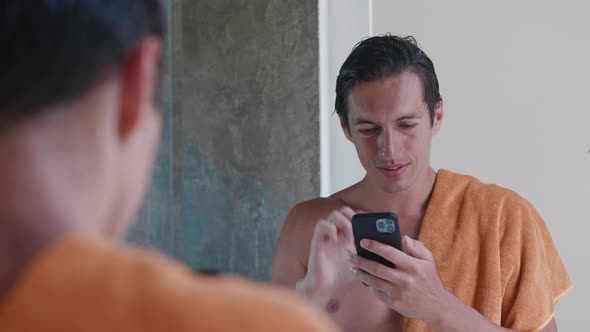 Portrait of Smiling Young Man with a Towel Stands in the Bathroom Standing in Front of a Mirror and