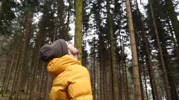 Caucasian man with hat and yellow jacket stares into treetops, circling shot.