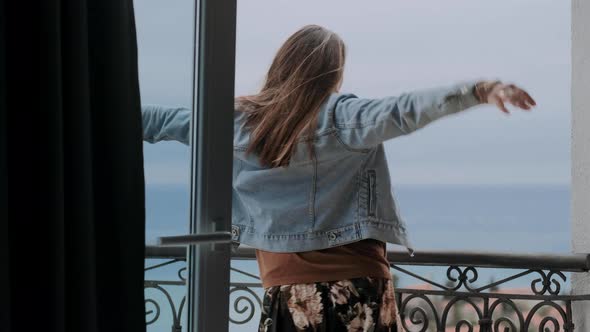 Young woman in a beige sweater stands on the balcony. Wind develops female’s hair, freedom concept