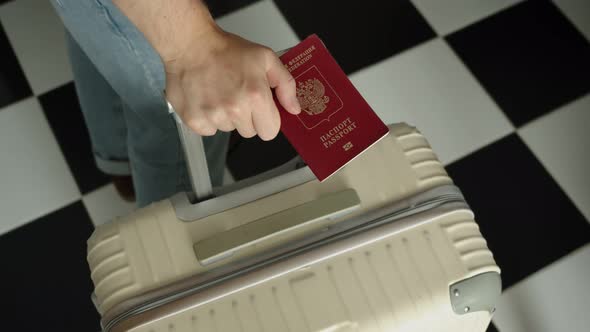 a Man with a Russian Passport in His Hand and a Suitcase Waits for His Flight at the Airport