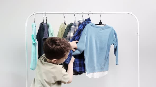 Boy preschooler standing by the hangers, racks up clothes, and chooses clothes for today.