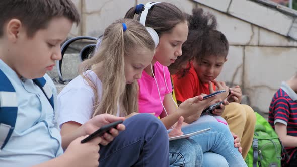 Schoolchildren Use Gadgets Resting on Steps After Lessons