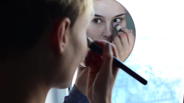 Woman Looking in the Mirror and Apply Makeup to the Face.