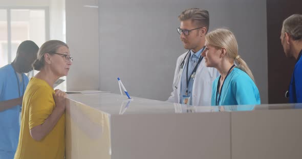 Senior Woman at Reception Desk in Clinic Filling in Medical Form