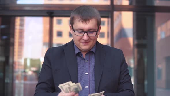 A Businessman Counts Money Standing Near the Business Center Having a Good Mood