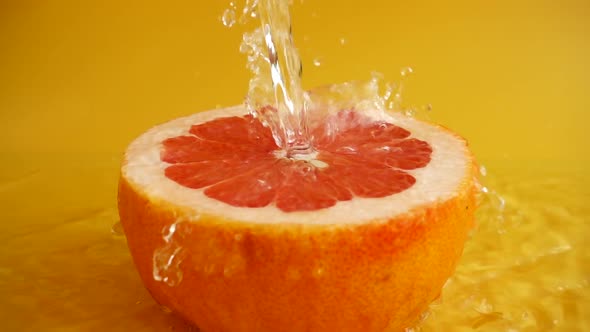 Half of a grapefruit in a jet of water on an orange background. Slow motion.