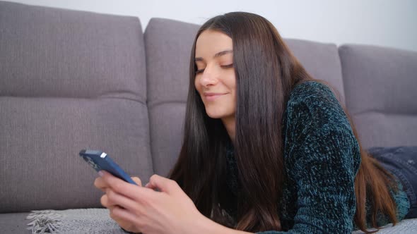 Cheerful white woman using mobile phone for online communication while lying down on couch at home